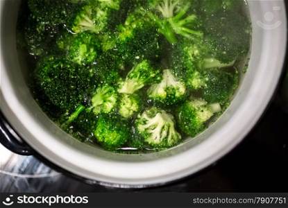 Closeup photo of broccoli boiling in white metal pan