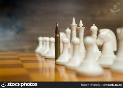 Closeup photo of bullet in row of white chess pieces on wooden board. Concept of military power
