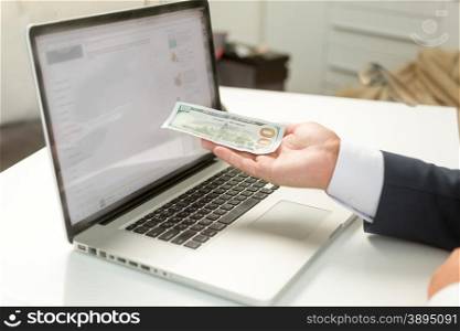 Closeup photo of businessman holding banknote on hand and giving it to computer