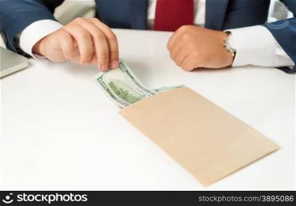 Closeup photo of businessman pulling banknote out of envelope lying on table