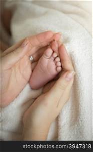 Closeup photo of caring mother holding newborn baby little feet