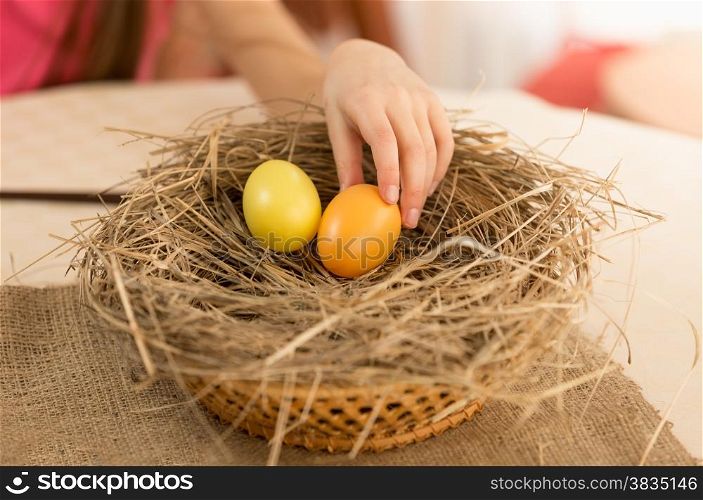 Closeup photo of child hand picking Easter egg from the nest