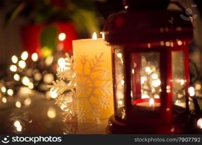 Closeup photo of Christmas lights, burning candle and vintage lantern on table