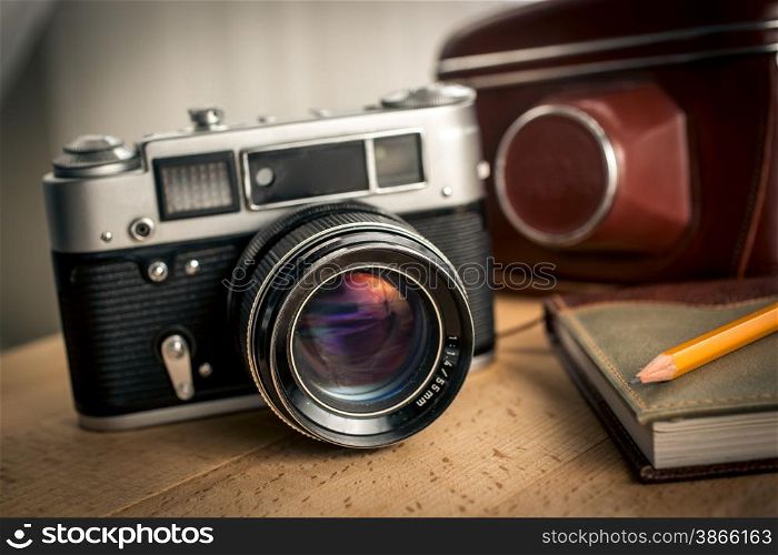 Closeup photo of classic film camera and notebook on wooden desk