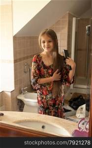 Closeup photo of cute small girl combing hair in front of mirror
