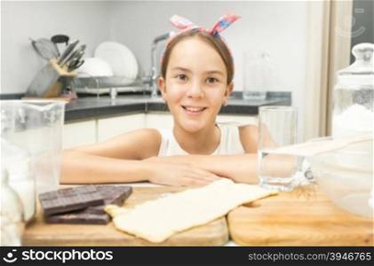 Closeup photo of cute smiling girl leaning on wooden cooking board on kitchen