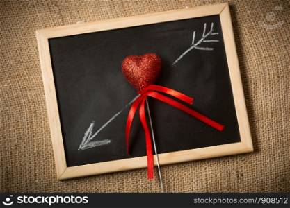 Closeup photo of drawn on chalkboard arrow going through decorative heart