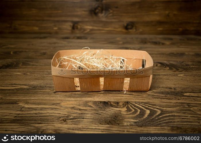 Closeup photo of empty little basket covered by straw lying on old wooden table