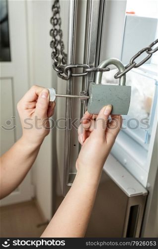 Closeup photo of female opening lock with chain on refrigerator