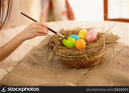 Closeup photo of girl holding paintbrush coloring Easter eggs