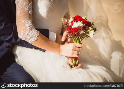 Closeup photo of groom hugging bride holding wedding bouquet