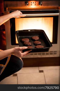 Closeup photo of housewife putting pan with cookies in oven