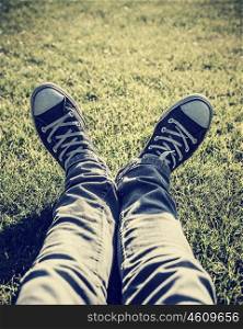 Closeup photo of lazy teen guy lying down on green grass an wearing stylish trendy gumshoes, body part, relaxing outdoors, sportive shoes, fashion for hipster