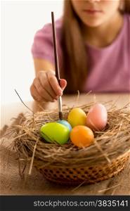 Closeup photo of little girl holding brush and painting Easter eggs in the nest