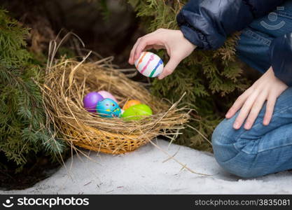 Closeup photo of little girl putting easter egg in nest at cold snowy day