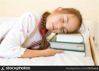 Closeup photo of little girl sleeping in bed on pile of books