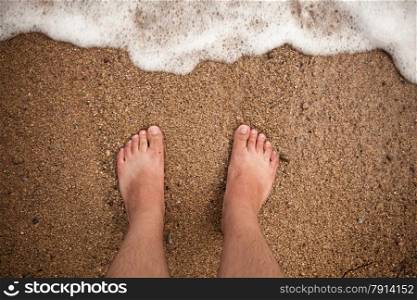 Closeup photo of male feet standing on sandy beach
