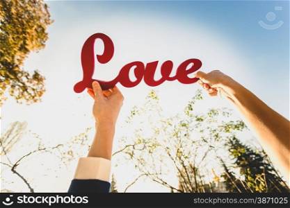 "Closeup photo of man and woman holding red "Love" sign"