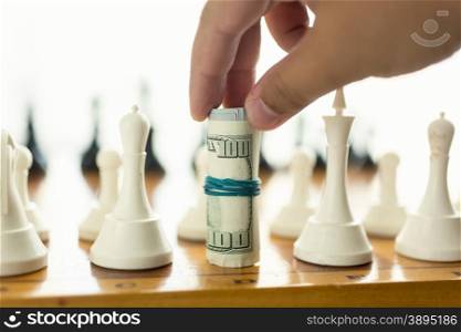 Closeup photo of man making move in chess game with twisted banknotes