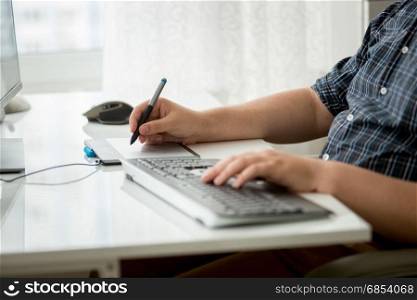 Closeup photo of man using digital graphic tablet and keyboard
