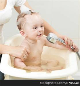 Closeup photo of mother bathing her cute baby in bathroom