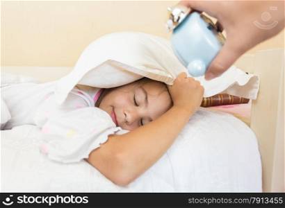 Closeup photo of mother holding alarm clock on sleeping daughters ear
