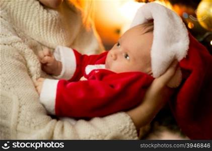 Closeup photo of mother holding baby boy in Santa costume and hat