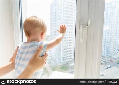 Closeup photo of mother holding baby boy while he is looking outside through window