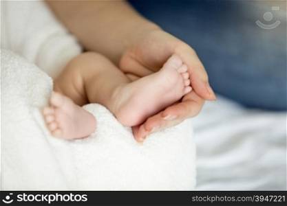 Closeup photo of mother holding newborn baby feet on bed