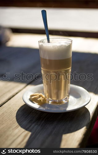 Closeup photo of of cappuccino in glass on wooden table at sunny day