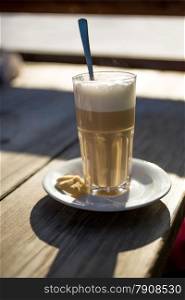 Closeup photo of of cappuccino in glass on wooden table at sunny day