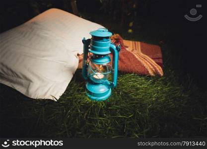 Closeup photo of old lantern, pillow and blanket lying on grass at night