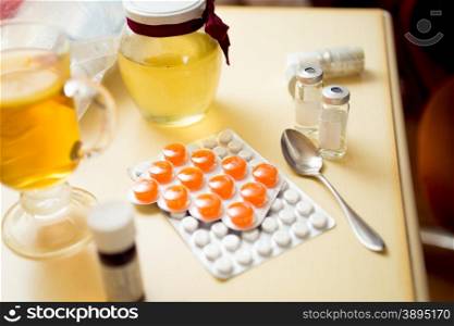 Closeup photo of pills in blister and honey jar on bedside table