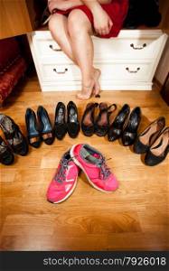 Closeup photo of pink sneakers among black high heeled shoes at wardrobe