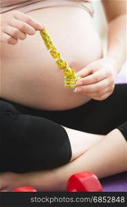 Closeup photo of pregnant woman holding measuring tape
