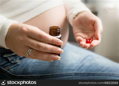 Closeup photo of pregnant woman holding red pill on hand