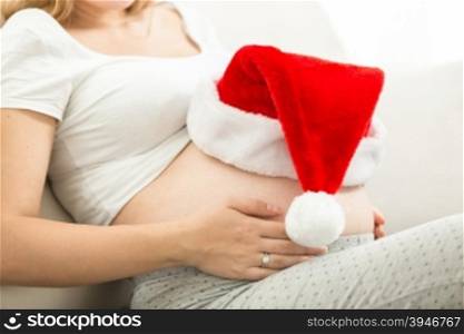 Closeup photo of pregnant woman holding Santa cap on tummy