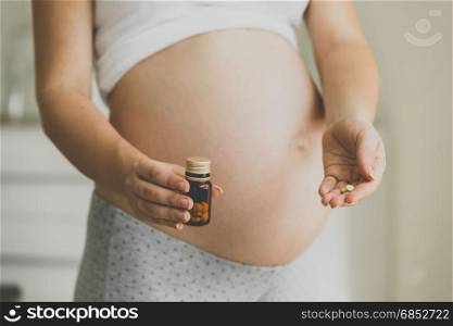 Closeup photo of pregnant woman holding vitamins in pills