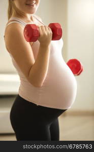 Closeup photo of pregnant woman lifting dumbbells