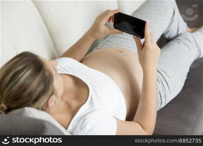 Closeup photo of pregnant woman lying on sofa and typing message