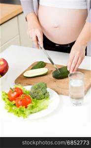 Closeup photo of pregnant woman making vegetable salad on kitchen