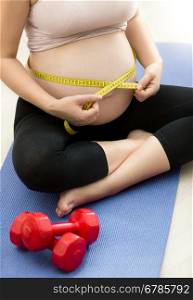 Closeup photo of pregnant woman measuring belly with tape