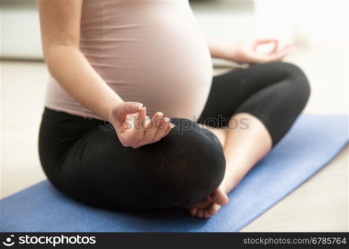 Closeup photo of pregnant woman meditating on floor at living room