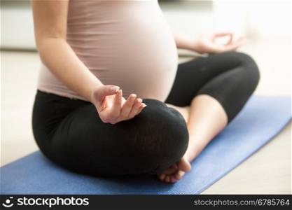 Closeup photo of pregnant woman meditating on floor at living room