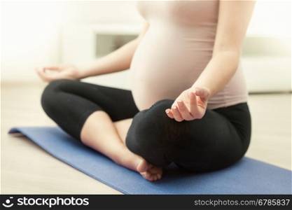 Closeup photo of pregnant woman practicing yoga at home