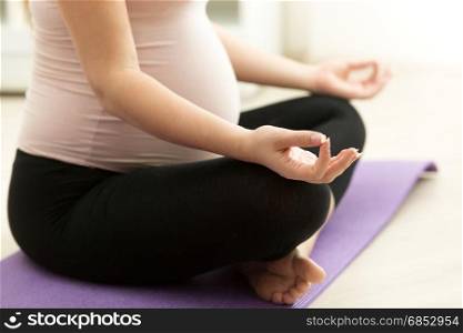 Closeup photo of pregnant woman practicing yoga on floor at home