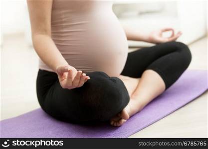 Closeup photo of pregnant woman sitting in yoga lotus position on floor
