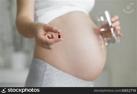 Closeup photo of pregnant woman with glass of water and pills
