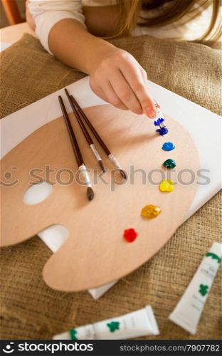 Closeup photo of professional artist squeezing oil paint from tubes on wooden pallet