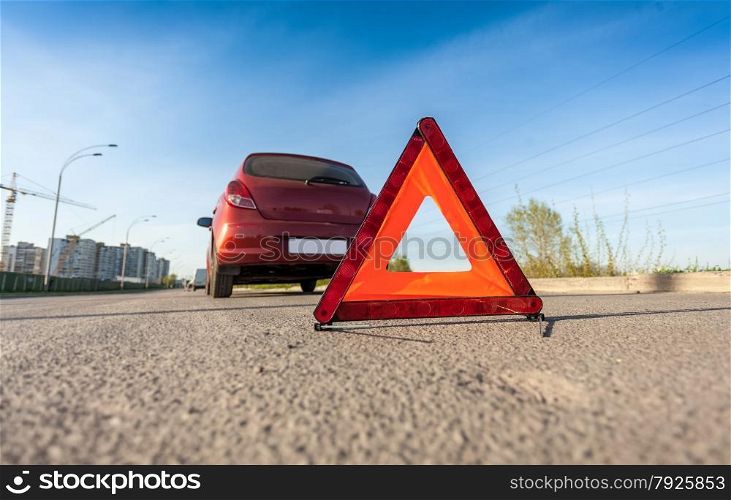 Closeup photo of red triangle sign on road next to broken car